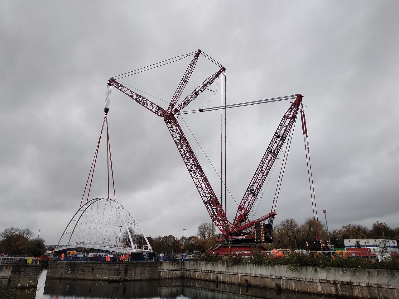Large crawler crane lifting an arch footbridge into place over a canal