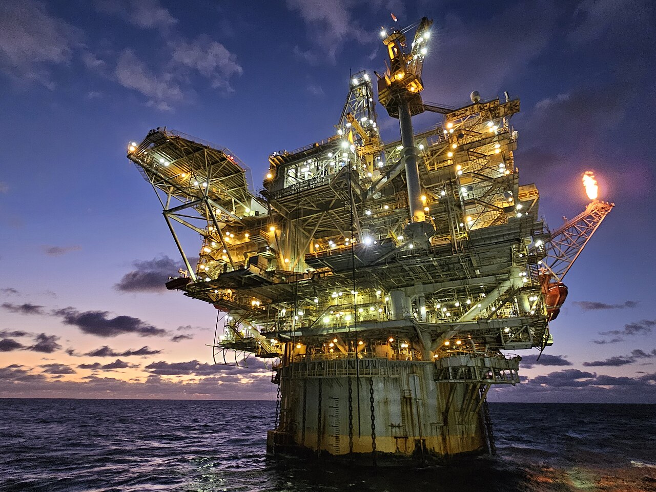 Offshore oil platform lit up at dusk, with its crane and mooring lines